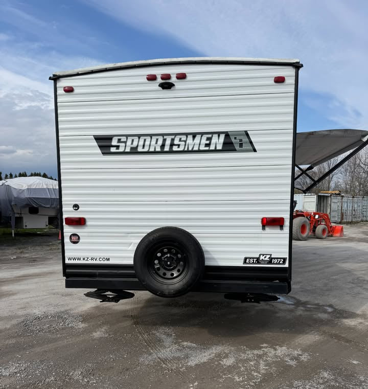 Back view of a Sportsmen RV trailer on a concrete surface with a clear sky.