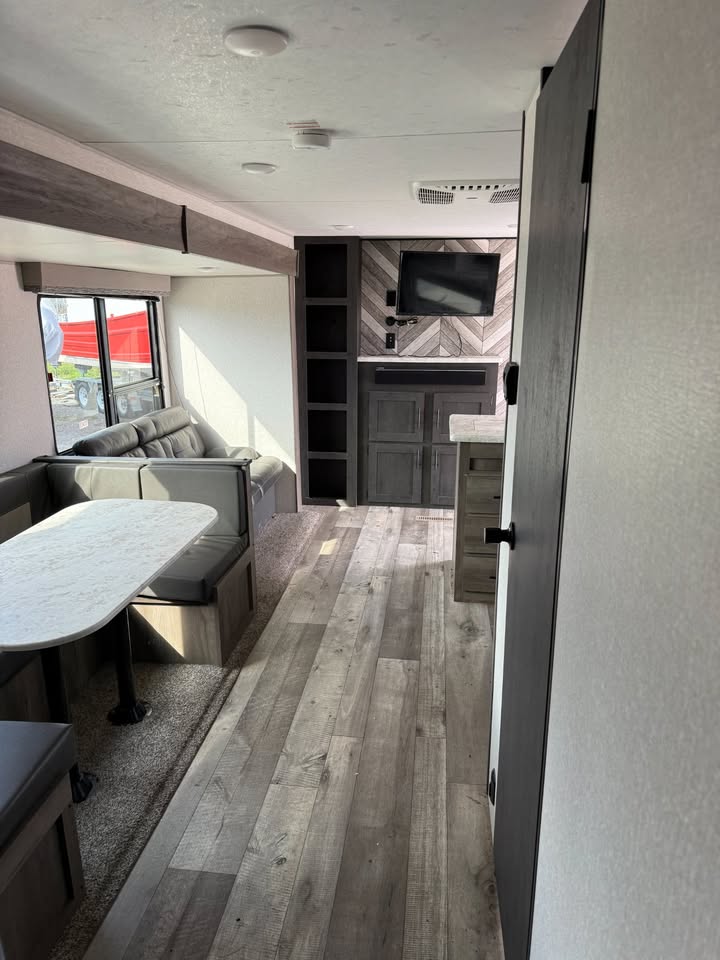 Interior of a modern RV with gray couch, kitchen area, and entertainment unit.