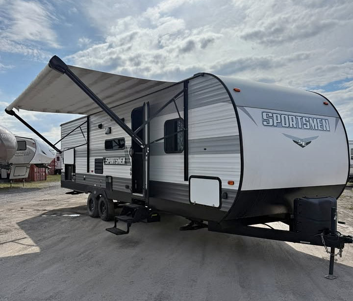 Travel trailer entrance door with an extended awning on a paved surface.