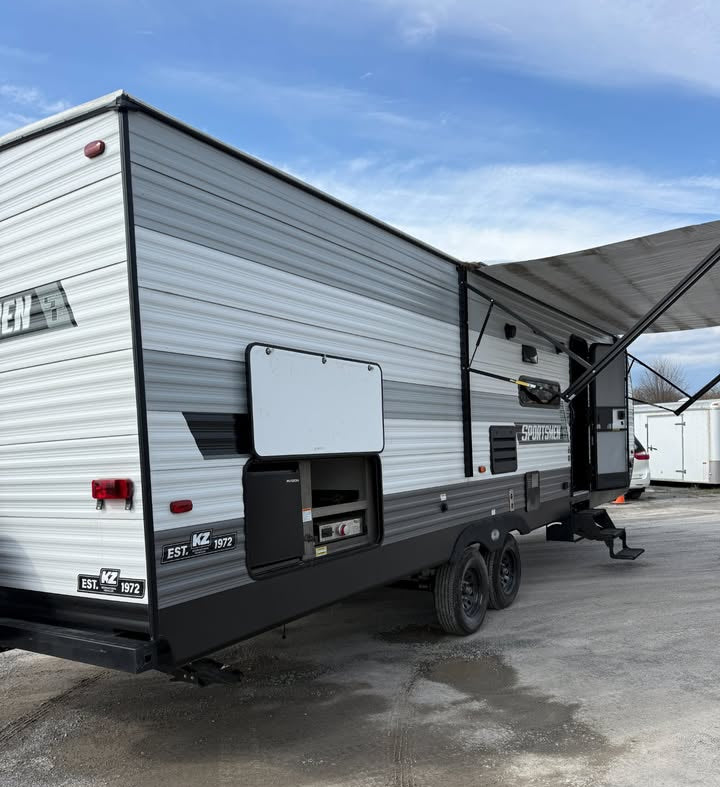 Gray and black travel trailer parked on a concrete surface with a blue sky in the background.