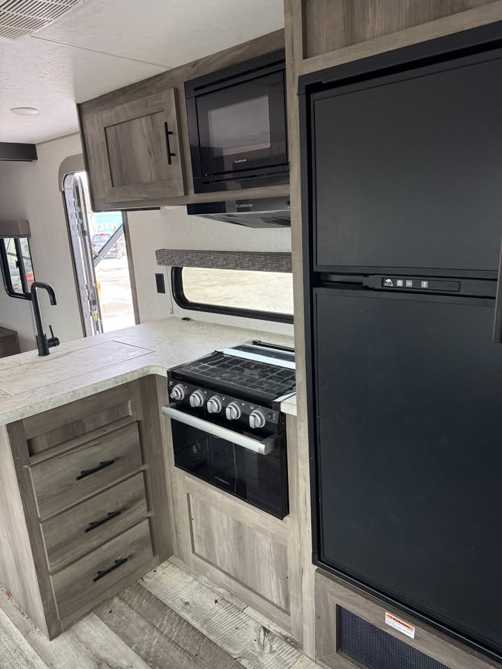 Compact kitchen area inside a recreational vehicle with stove, oven, and refrigerator.