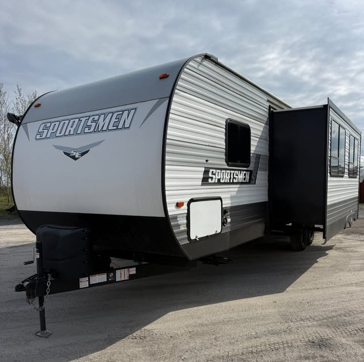 Gray Sportsmen travel trailer with an open door on a paved surface.