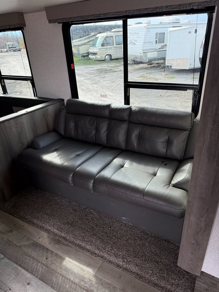 Gray sofa inside a vehicle with large windows showing an exterior view of another vehicle.